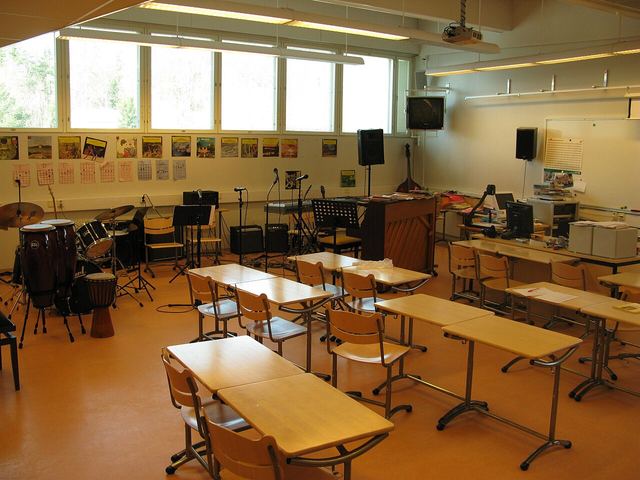 A school music room with a drum kit, a piano and rows of desks.