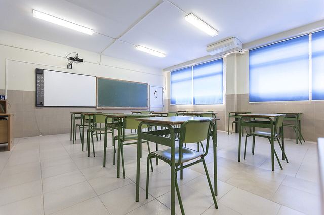 A bright classroom with rows of desks, a whiteboard and large windows.