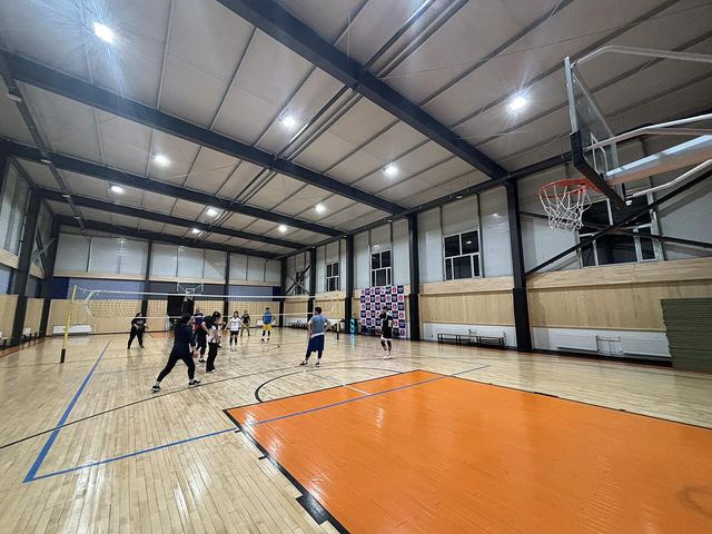 An indoor sports hall with a wooden floor, a basketball hoop and a volleyball net.